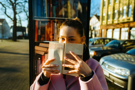 Portrait of young caucasian woman college student hiding behind a book and looking at camera.の写真素材