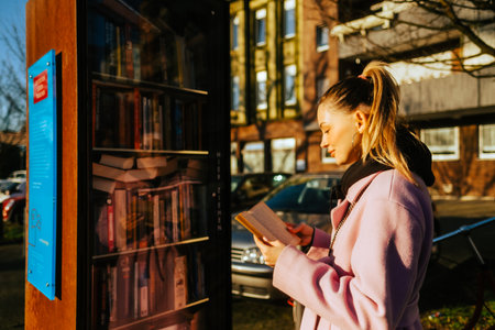 Young caucasian woman choosing books at free open public library at city park for book sharing among readers.の写真素材