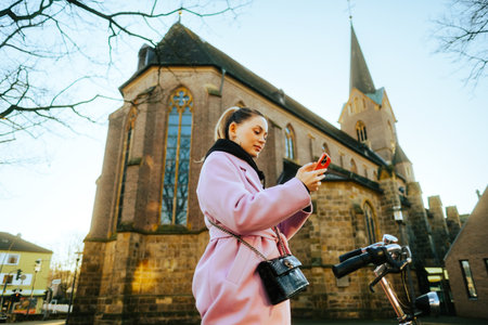 Young attractive caucasian woman using mobile phone, ride on bicycle in the city street.の写真素材