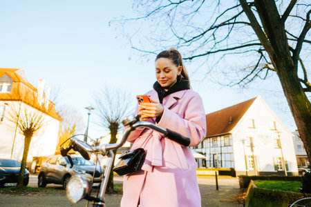 Young attractive caucasian woman using mobile phone, ride on bicycle in the city street.の写真素材