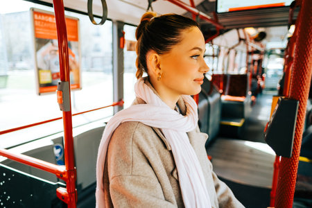 An attractive caucasian woman riding in a bus in the sunny day. Young beautiful woman using public transportation.の写真素材