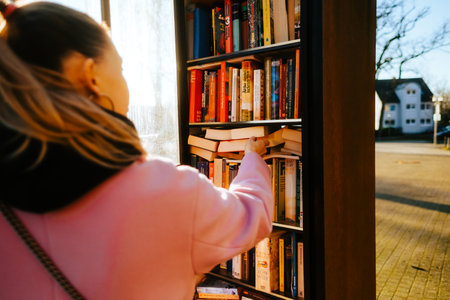 Young caucasian woman choosing books at free open public library at city park for book sharing among readers.の写真素材