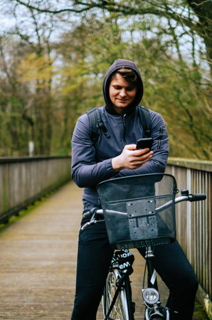 Young caucasian man cyclist ride on bicycle in the park and using mobile phone.の写真素材