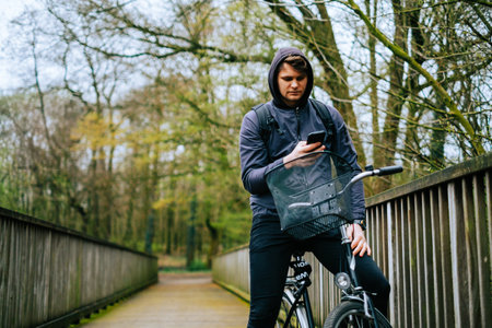 Young caucasian man cyclist ride on bicycle in the park and using mobile phone.の写真素材