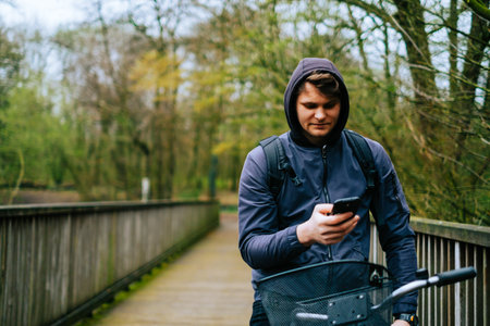Young caucasian man cyclist ride on bicycle in the park and using mobile phone.の写真素材