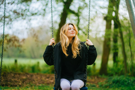 Joyful and youthful woman on a swing at the park. Concept pf people and no limit age to play and have fun. Female in outdoor leisure activity using swing and enjoy lifeの写真素材