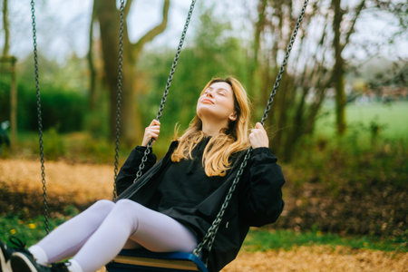 Joyful and youthful woman on a swing at the park. Concept pf people and no limit age to play and have fun. Female in outdoor leisure activity using swing and enjoy lifeの写真素材