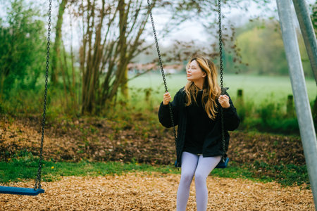 Joyful and youthful woman on a swing at the park. Concept pf people and no limit age to play and have fun. Female in outdoor leisure activity using swing and enjoy lifeの写真素材