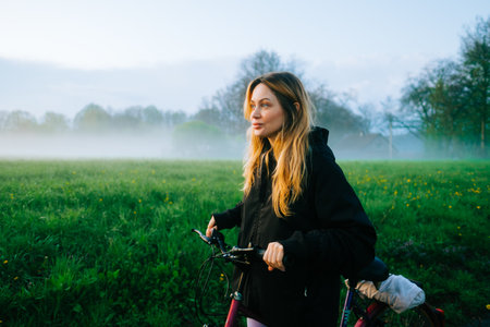 Young attractive caucasian woman ride on bicycle in the park in sunset with fog, beautiful scenic view .の写真素材