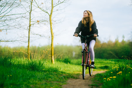 Portrait of young attractive woman riding on bicycle in the park in springtime.の写真素材
