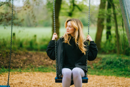 Joyful and youthful woman on a swing at the park. Concept pf people and no limit age to play and have fun. Female in outdoor leisure activity using swing and enjoy lifeの写真素材