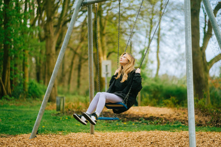 Joyful and youthful woman on a swing at the park. Concept pf people and no limit age to play and have fun. Female in outdoor leisure activity using swing and enjoy lifeの写真素材