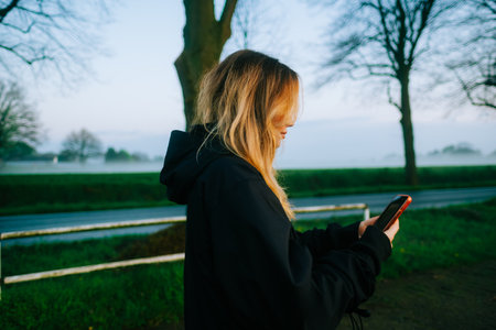 Young attractive caucasian woman using mobile phone, ride on bicycle in the park in sunset with fog .の写真素材