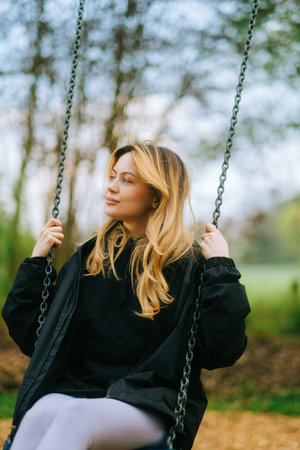 Joyful and youthful woman on a swing at the park. Concept pf people and no limit age to play and have fun. Female in outdoor leisure activity using swing and enjoy lifeの写真素材