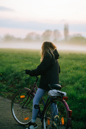 Young attractive caucasian woman ride on bicycle in the park in sunset with fog, beautiful scenic view .の写真素材