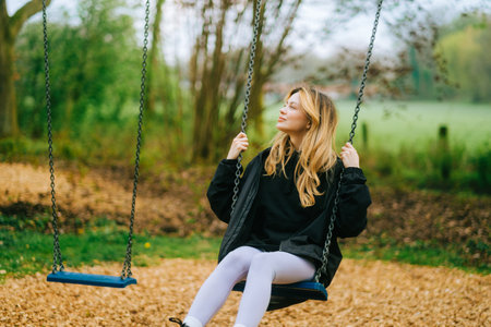 Joyful and youthful woman on a swing at the park. Concept pf people and no limit age to play and have fun. Female in outdoor leisure activity using swing and enjoy lifeの写真素材