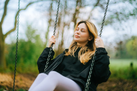 Joyful and youthful woman on a swing at the park. Concept pf people and no limit age to play and have fun. Female in outdoor leisure activity using swing and enjoy lifeの写真素材