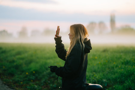 Young attractive caucasian woman making photo of beautiful view of sunset with fog while ride on bicycle in the park .の写真素材