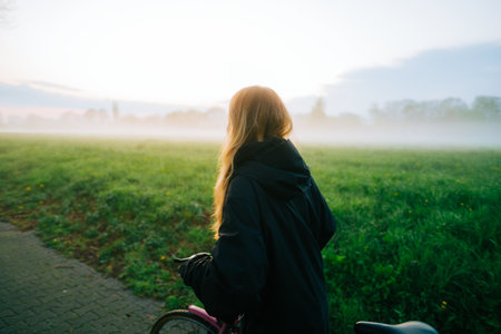 Young attractive caucasian woman ride on bicycle in the park in sunset with fog, beautiful scenic view .の写真素材