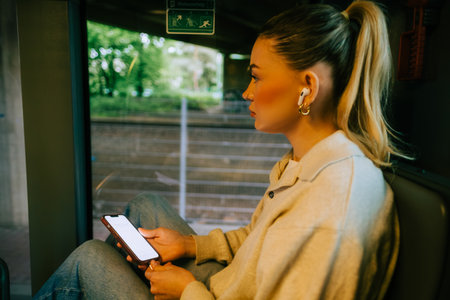 An attractive caucasian woman using a smartphone in a city bus. Young beautiful woman using public transportation.の写真素材