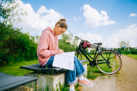 Young attractive caucasian woman student making home work outdoors on a bench in a park.の写真素材