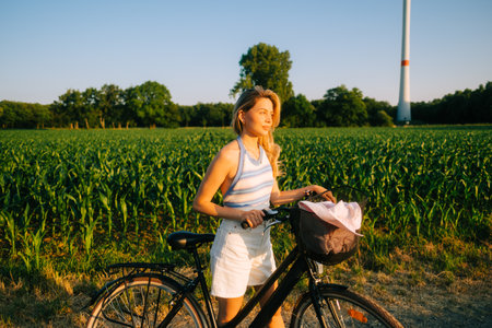 Portrait of young attractive woman with bike at the countryside field in sunset.の写真素材