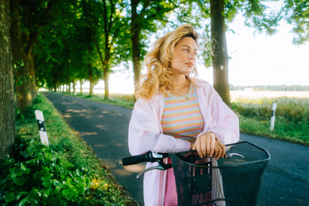 Portrait of young caucasian woman with blond hair riding on bicycle among agricultural fields in countryside in summer day.の写真素材