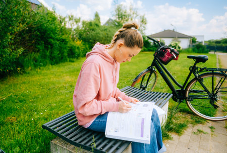 Young attractive caucasian woman student making home work outdoors on a bench in a park.の写真素材