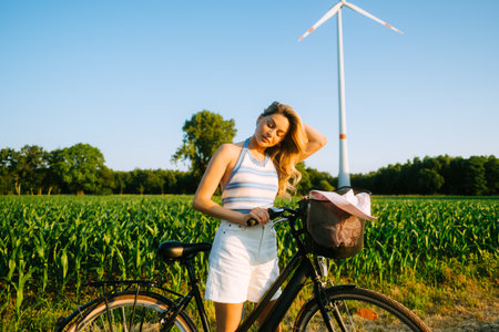 Portrait of young attractive woman with bike at the countryside field in sunset.の写真素材
