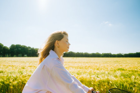 Young caucasian woman with blond hair riding among agricultural fields in countryside in summer day.の写真素材