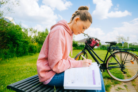 Young attractive caucasian woman student making home work outdoors on a bench in a park.の写真素材