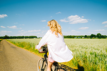 Young caucasian woman with blond hair riding among agricultural fields in countryside in summer day.の写真素材
