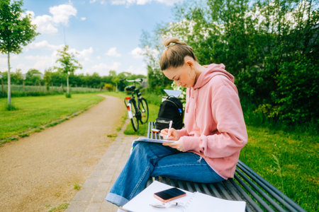 Young attractive caucasian woman student making home work outdoors on a bench in a park.の写真素材