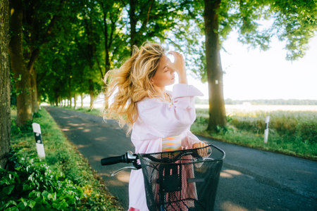 Portrait of young caucasian woman with blond hair riding on bicycle among agricultural fields in countryside in summer day.の写真素材