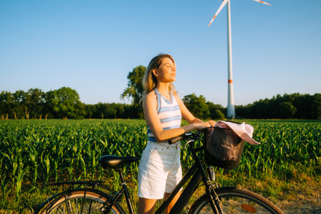Portrait of young attractive woman with bike at the countryside field in sunset.の写真素材