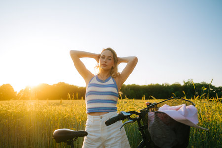 Portrait of young attractive woman with bike at the countryside field in sunset.の写真素材