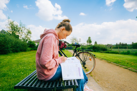 Young attractive caucasian woman student making home work outdoors on a bench in a park.の写真素材