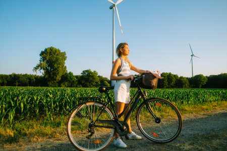 Portrait of young attractive woman with bike at the countryside field in sunset.の写真素材