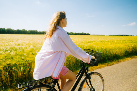Young caucasian woman with blond hair riding among agricultural fields in countryside in summer day.の写真素材