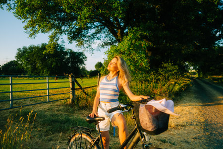 Young attractive caucasian woman with bicycle near horses pasture in summer day at sunset.の写真素材