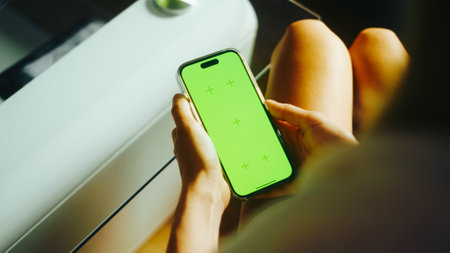 Young woman sitting on sofa at home and uses mobile phone with green screen Mock-up.の写真素材
