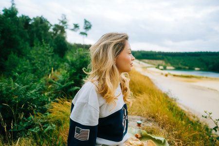 Portrait of attractive caucasian woman making picnic near forest lake, calm and enjoying natureの写真素材