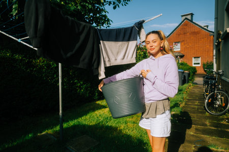 Young caucasian woman hanging clothes on washing line outdoor for drying on the backyard.の写真素材