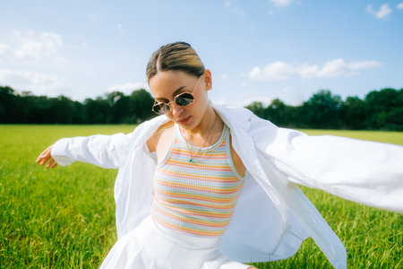 Portrait of young attractive caucasian woman, fashion model posing on a green countryside field in sunny summer day, enjoying the weather.の写真素材