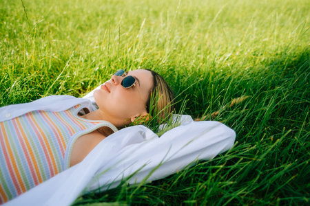 Beautiful caucasian woman in sunglasses lying down of grass in summer sunny day.