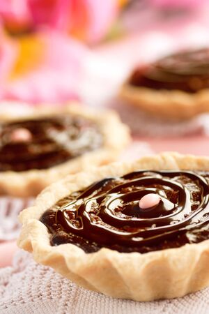 Delicious chocolate tarts with chocolate frosting and pink background.の写真素材