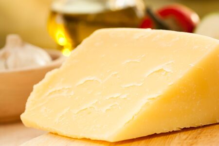 Big slice of cheese with vegetables in the backの写真素材