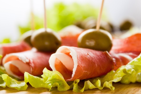 Slices of prosciutto rolled up and arranged on a lettuce leaf. Shallow depth of field.の写真素材