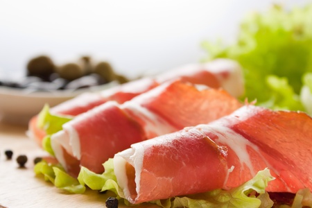 Slices of prosciutto rolled up and arranged on a lettuce leaf. Shallow depth of field.