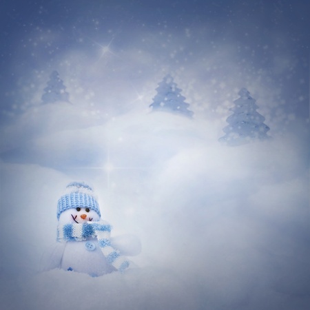 Christmas blue background. Snowman toy on the bokeh winter background in the snow and magical forest with Christmas shiny trees.の写真素材